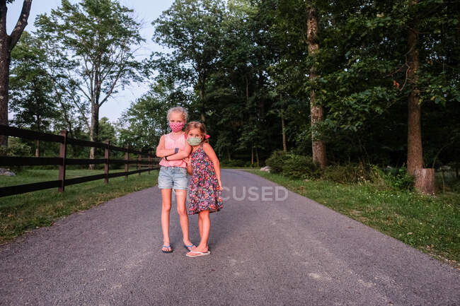 Retrato de dos niñas con máscaras en la carretera en el bosque en verano - foto de stock