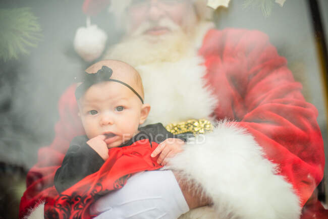 Baby sitzt auf dem Schoß des Weihnachtsmanns im Fenster — Stockfoto
