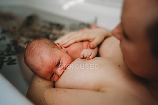 Bebê recém-nascido amamentando na banheira enquanto a mãe toca suas costas — Fotografia de Stock