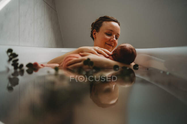 Reflection on water of happy mum nursing newborn baby in bath tub — Stock Photo