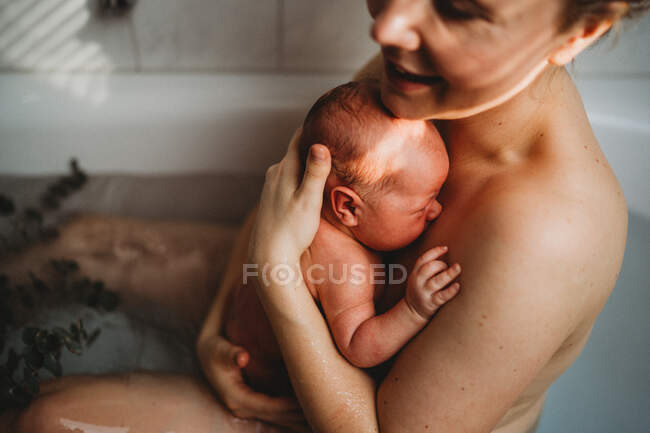 Счастливая улыбающаяся мать, держащая своего новорожденного ребенка после рождения дома — стоковое фото