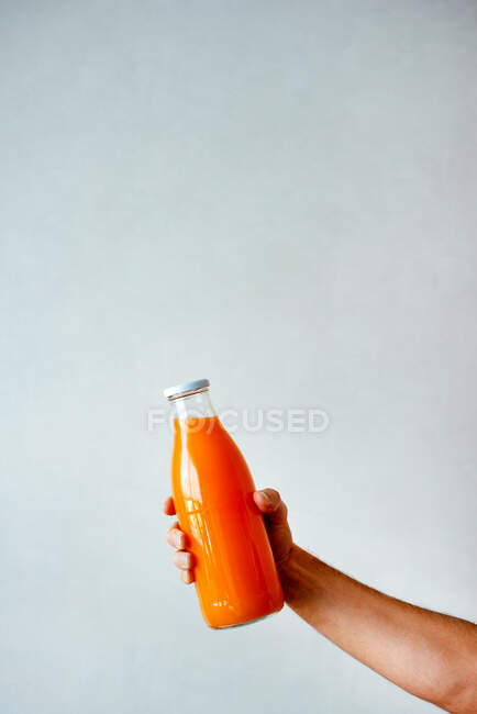 Female hand holding orange bottle with fresh fruits on color background — Stock Photo