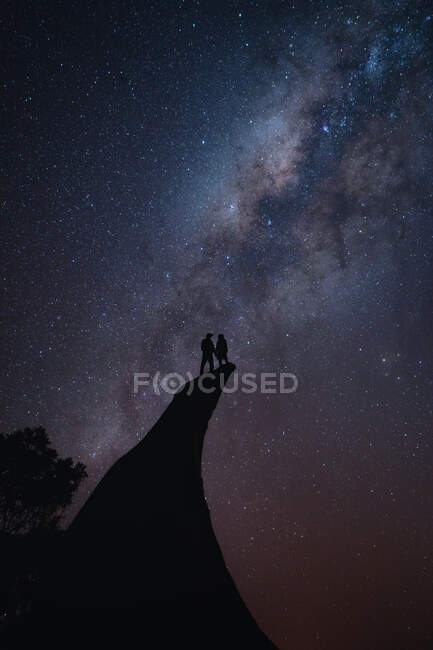 Casal de pé na beira de um penhasco durante o céu noturno — Fotografia de Stock