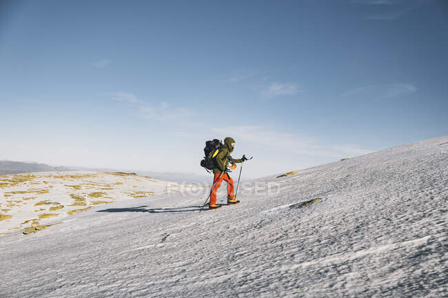 Молодой мужчина поднимается в гору на снегу против ясного голубого неба, Гредос, Авила, Испания — стоковое фото