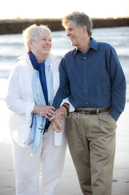 Портрет літньої подружньої пари, що тримається за руки і сміється на пляжі. — стокове фото