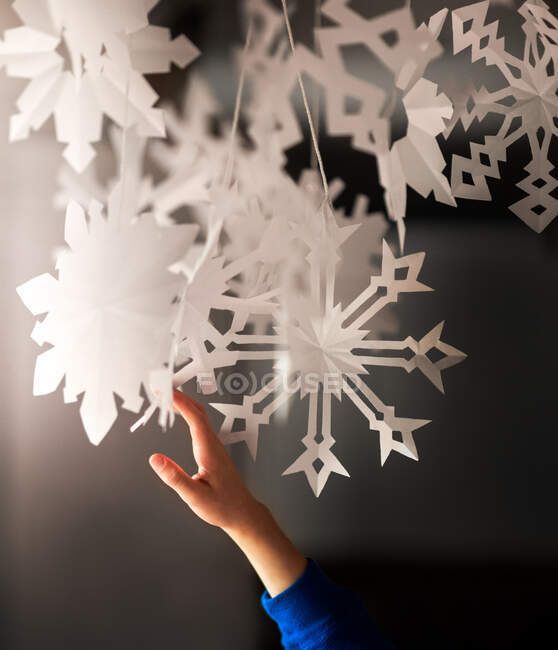 Una mano che raggiunge fino a toccare fiocchi di neve di carta davanti a una finestra — Foto stock