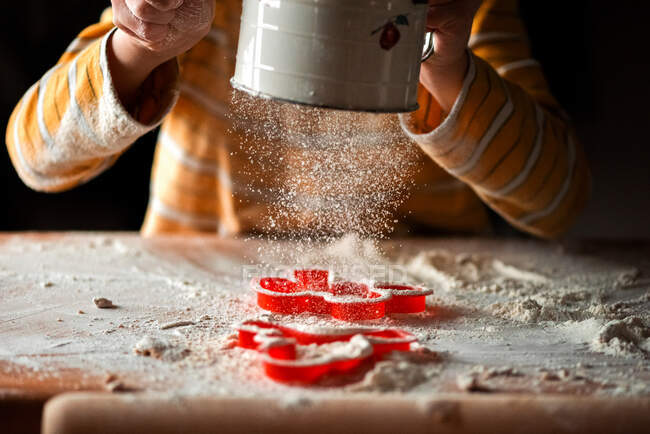 Дитина використовує борошно розріджувач над обробною дошкою та різаками для печива — стокове фото
