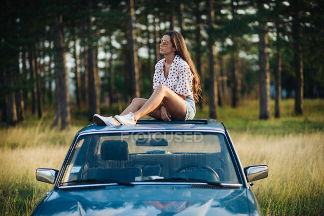 Uma mulher sentada no telhado de um carro. — Fotografia de Stock