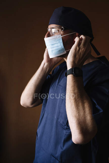 Médico masculino hispano poniéndose mascarilla. - foto de stock