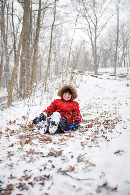 Glücklicher Junge, der an einem verschneiten Wintertag einen Hügel im Wald hinunterrodelt. — Stockfoto
