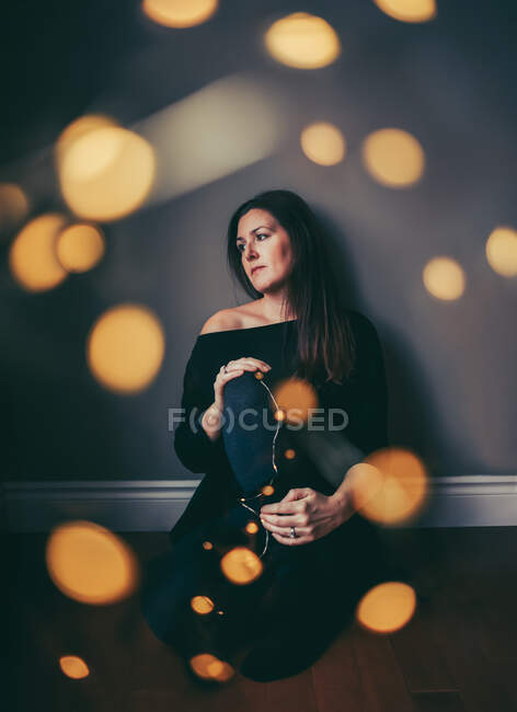 Pensive pretty woman sitting on floor with light bokeh surrounding her — Stock Photo