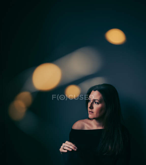 Pensive hübsche Frau in dunklen Raum mit hellen Bokeh um sie herum — Stockfoto