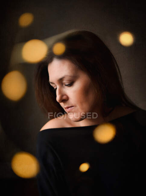 Pensive pretty woman in dark room with light bokeh surrounding her — Stock Photo
