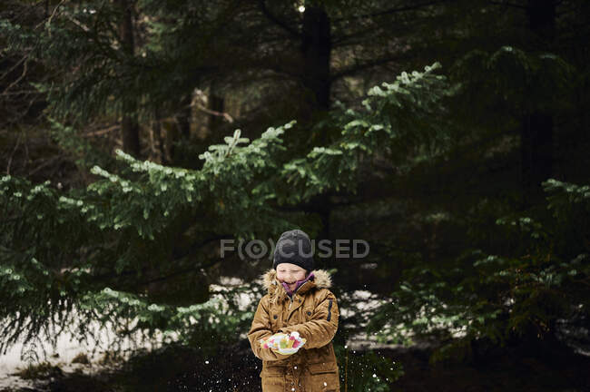 Bambino felice che fa la palla di neve vicino ad abete in foresta — Foto stock