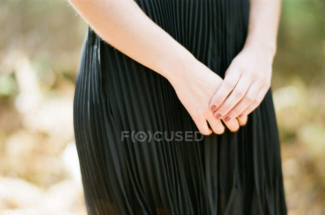Mulher de mãos dadas na frente do corpo em vestido com fundo simples — Fotografia de Stock