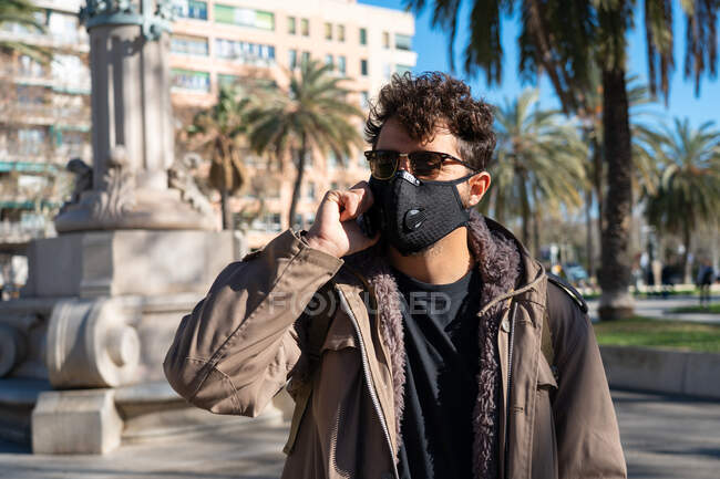 Чоловік з маскою обличчя і сонцезахисними окулярами, що викликають по телефону на вулиці — стокове фото