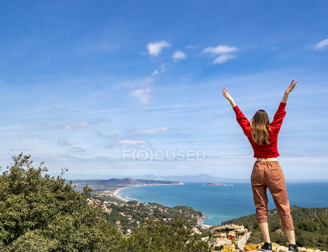 Веселая девушка, одетая в красное, наслаждается побережьем и смотрит на море — стоковое фото