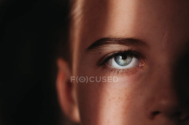 Close up of child's blue eye with black background in beam of light — Stock Photo
