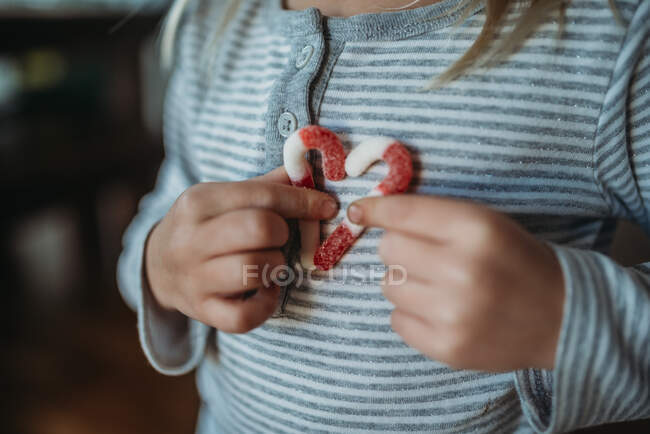 Cropped hands of girl holding candy canes in a heart on her chest — Stock Photo