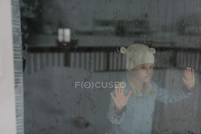 Petite fille regardant par la grande fenêtre à la neige — Photo de stock