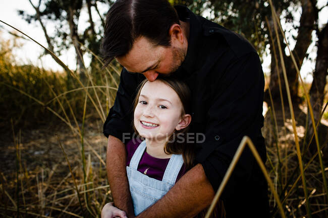 Papá besando a la hija en la parte superior de la cabeza en el parque en Chula Vista - foto de stock