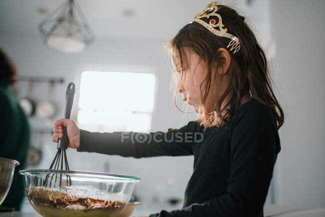 Preschool age girl in tiara baking with mixing bowl and whisk — Stock Photo