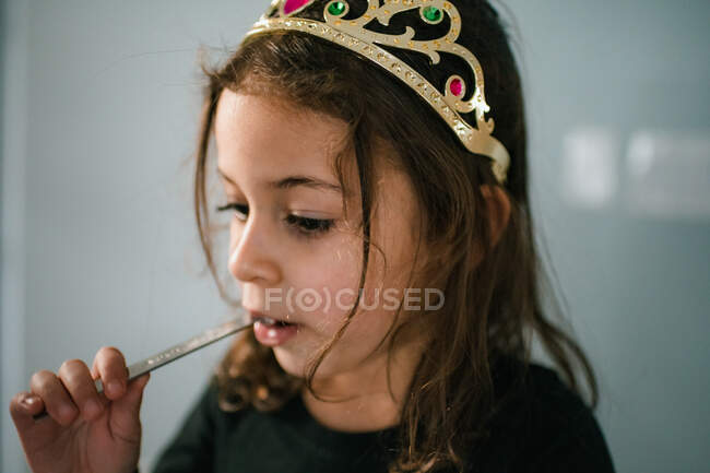 4 year old girl wearing tiara and eating from measuring spoon — Stock Photo