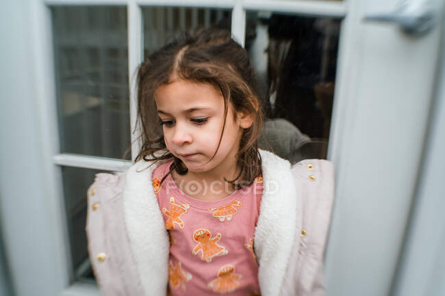 Girl in christmas pajamas rests against door outside — Stock Photo
