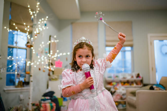 Chica joven jugando a vestir cantando en el micrófono con el árbol de Navidad - foto de stock