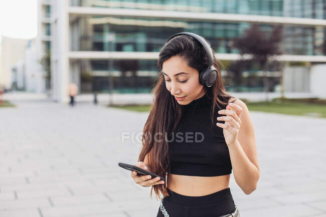 Молода жінка в чорному з навушниками дивиться на її смартфон — стокове фото