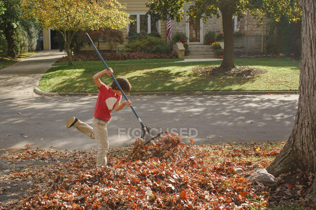 Хлопчик з ентузіазмом ламає листя в теплий осінній день надворі — стокове фото