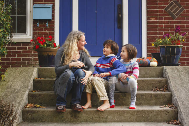 A smiling Mom sits with her two children on front stoop of home — Stock Photo