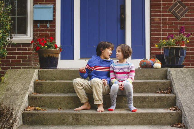 A brother and sister sit smiling together on front stoop of home — Stock Photo