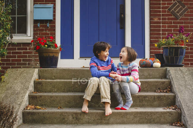 Мальчик и девочка, сидящие на крыльце, громко кричат от радости вместе — стоковое фото