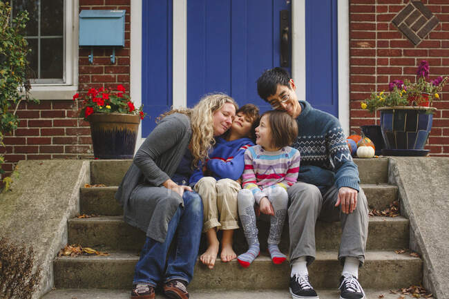 Una familia amorosa se acurrucan juntos en el frente de la casa en otoño - foto de stock