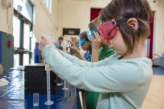 Une petite fille en lunettes de sécurité mesure le liquide dans un tube à essai — Photo de stock