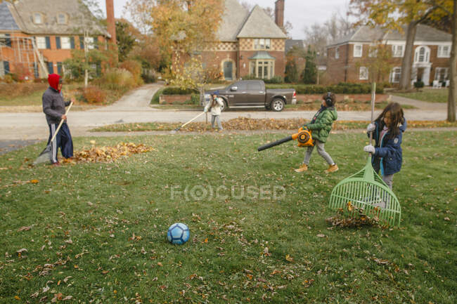 Трое детей помогают отцу убирать листья со двора осенью. — стоковое фото