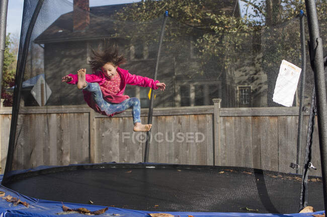 Une joyeuse petite fille aux cheveux sauvages saute sur le trampoline avec filet en filet — Photo de stock