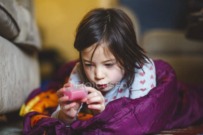 A little girl lays on floor in sleeping bag studying a tube of liquid — Stock Photo