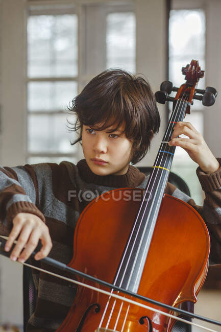 Primo piano di preteen boy con espressione seria che suona il violoncello a casa — Foto stock