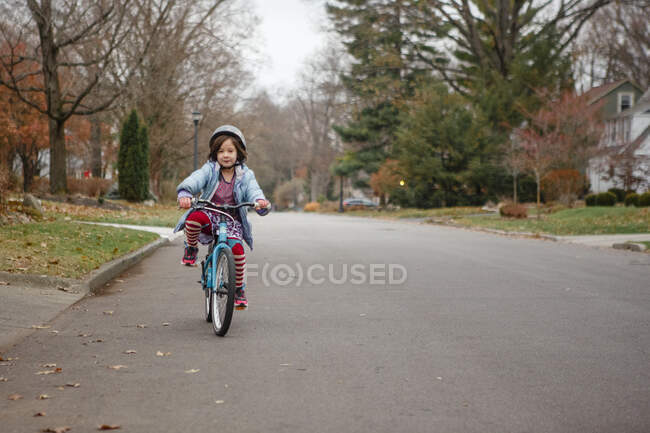 Ein kleines Mädchen in gestreiften Strumpfhosen und Helm radelt allein die Straße hinunter — Stockfoto