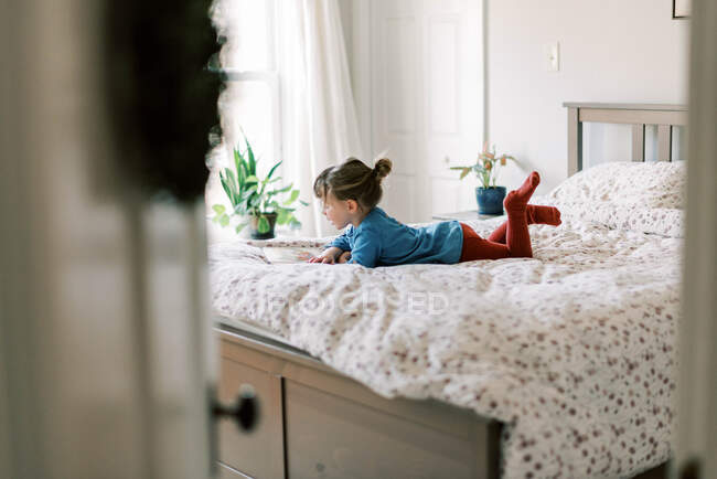 Pequeña niña independiente en la cama leyendo un libro de cuentos sola - foto de stock