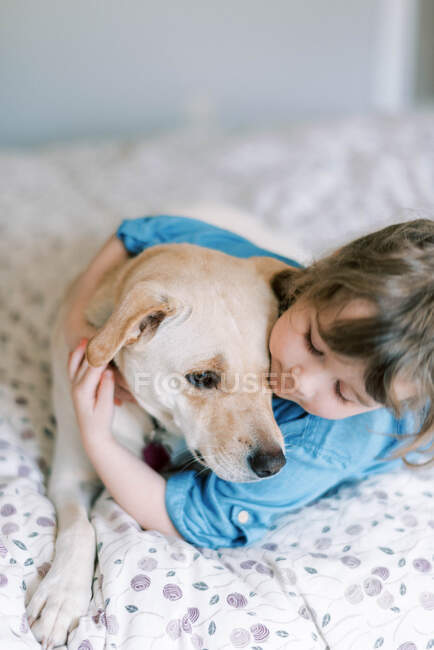 Sweet moment between caring gentle toddler girl and dog on bed — Stock Photo