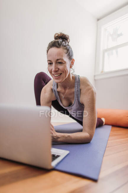 Женщина практикует йогу с ноутбуком у себя дома — стоковое фото