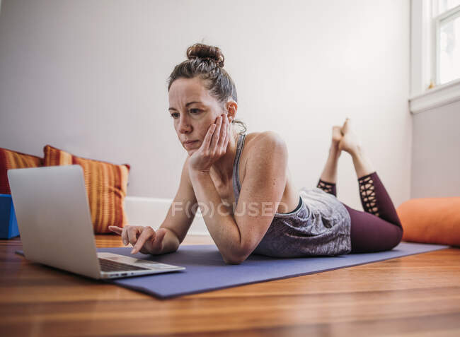 Женщина практикует йогу с ноутбуком у себя дома — стоковое фото