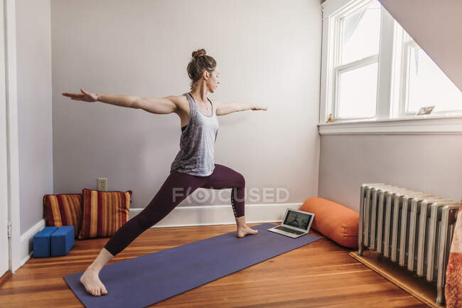 Mulher praticando ioga com computador portátil em sua casa — Fotografia de Stock