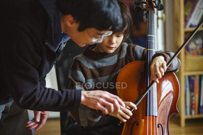 A father leans in to help his son properly hold a cello bow — Stock Photo