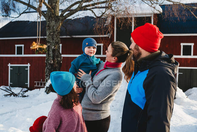 Happy family gathered by red Scandinavian bar in cold winter with snow — Stock Photo