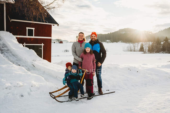 Happy smiling family in snowy countryside farm during sunset — Stock Photo