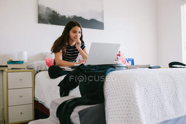 Tra ragazza works su suo computer portatile mentre su suo letto durante online scuola — Foto stock
